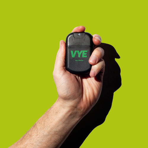 Hand holding a black VYE sprayer against a lime green background, Citrus flavour.