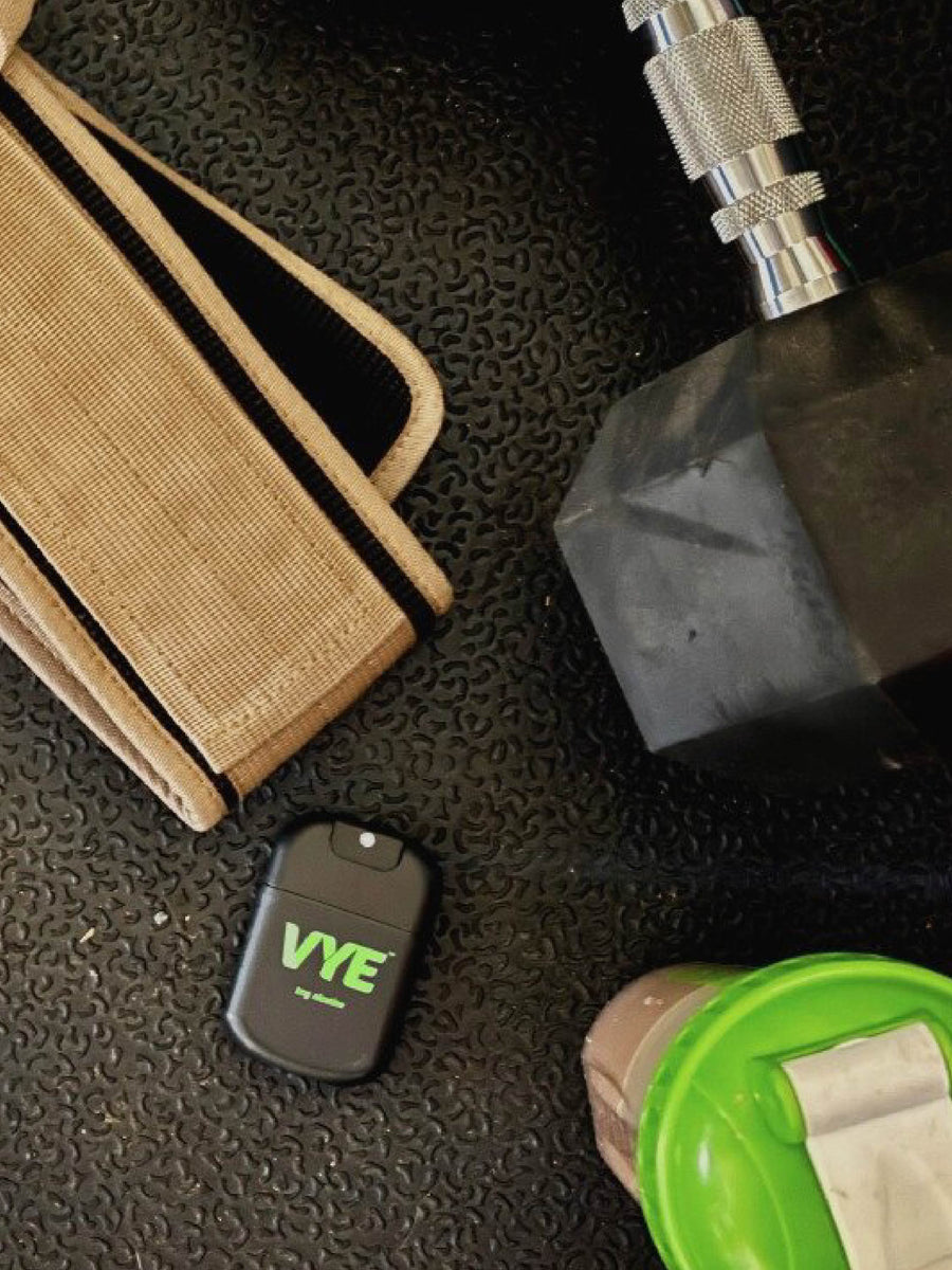 A VYE mist device sits beside a green bottle and folded dark clothing.